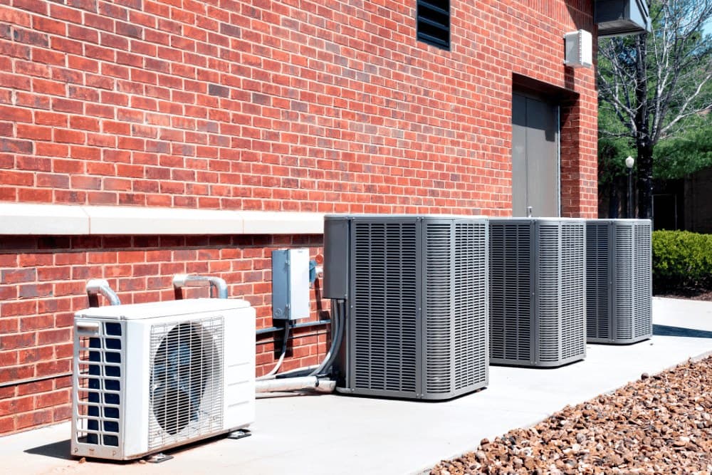Row of large outdoor condenser units and a wall-mounted split unit beside a brick building, the kind of multi-zone VRV equipment diagnosed on Daikin systems