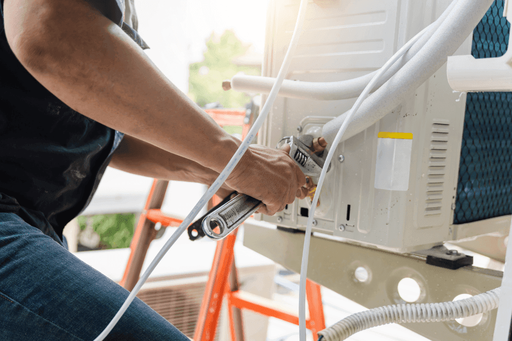 Technician tightening a refrigerant line fitting on an outdoor air conditioner unit with a wrench