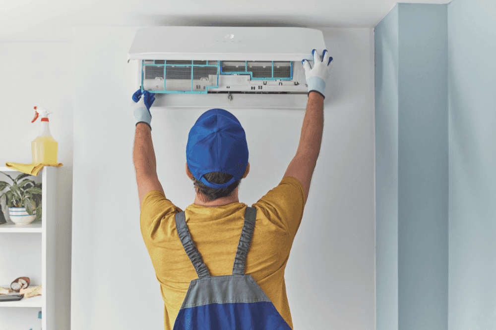 Technician wearing gloves lifting the front panel of a split air conditioner to clean the filter