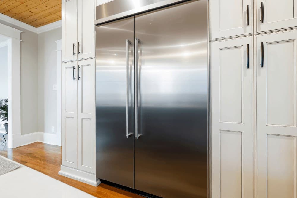 Large built-in stainless steel double-door refrigerator set into white cabinetry in a kitchen with a wood floor