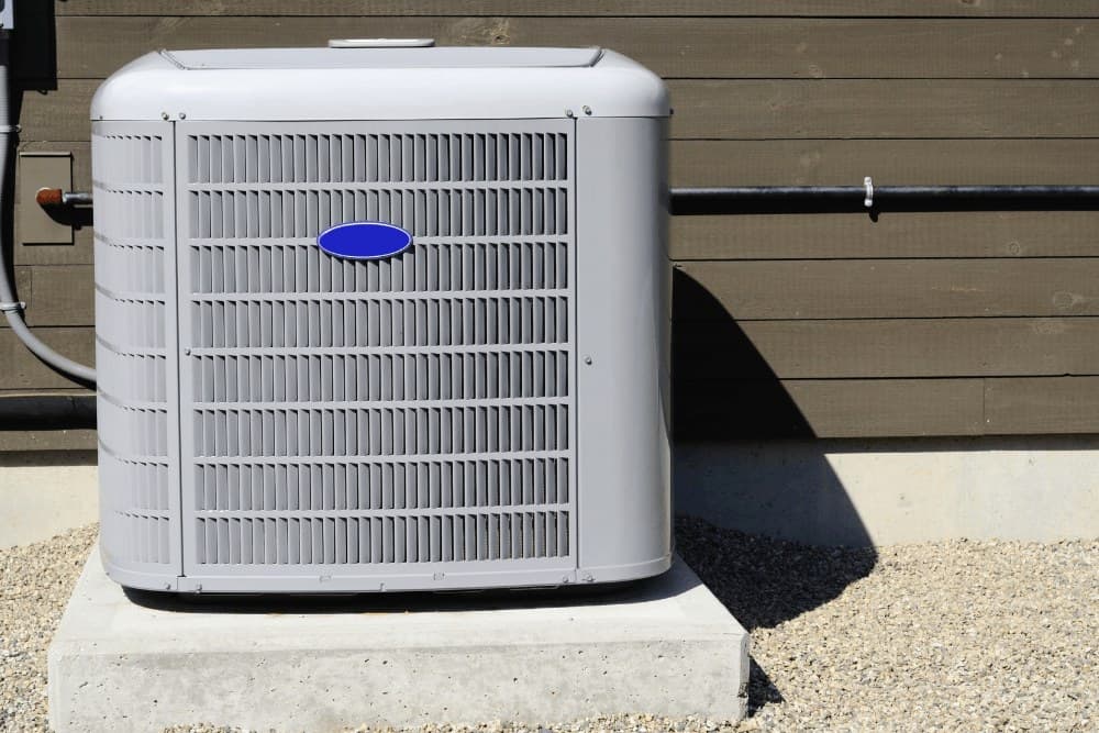 Carrier outdoor air conditioner condenser unit installed on a concrete pad beside a timber wall