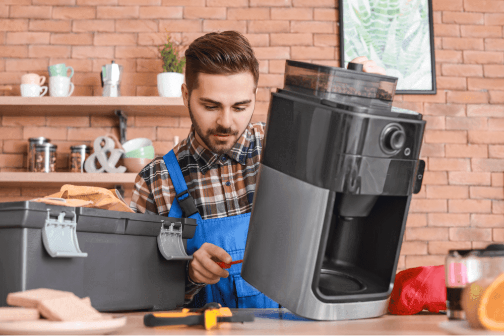 Technician inspecting a coffee machine on a café counter with an open toolbox beside him