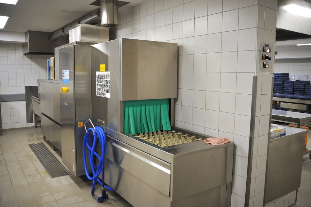 Commercial stainless steel tunnel dishwasher in a restaurant back-of-house kitchen, one of the commercial appliances we repair