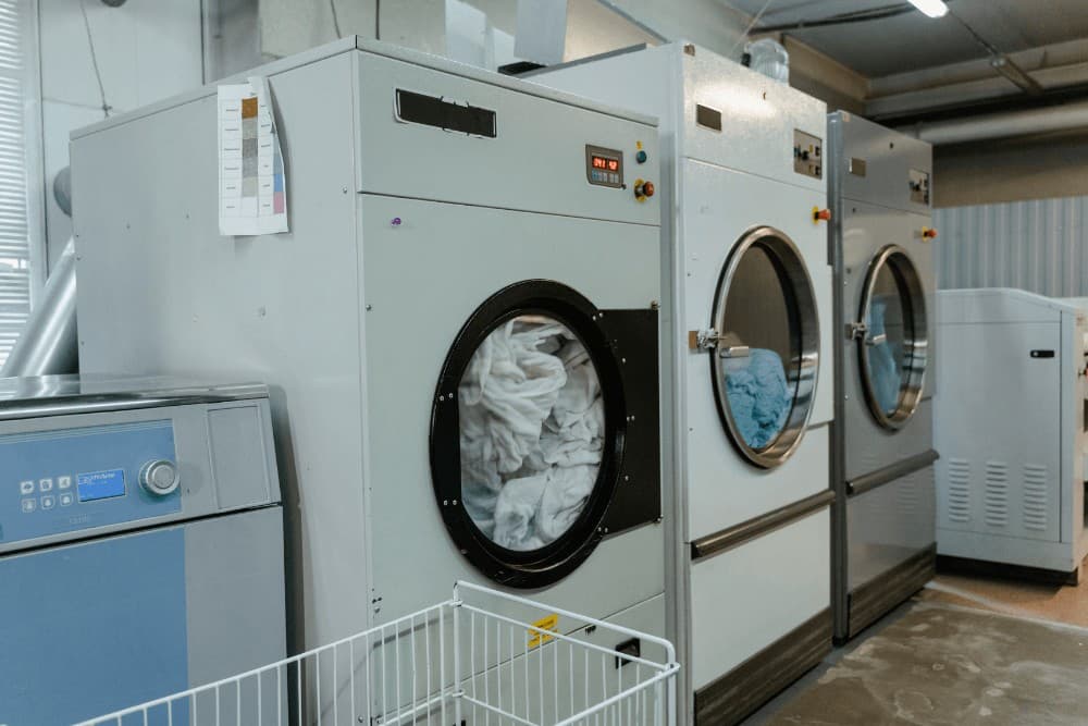 Row of stacked commercial industrial dryers in a laundromat or back-of-house laundry facility, the kind of equipment serviced under a commercial laundry maintenance contract