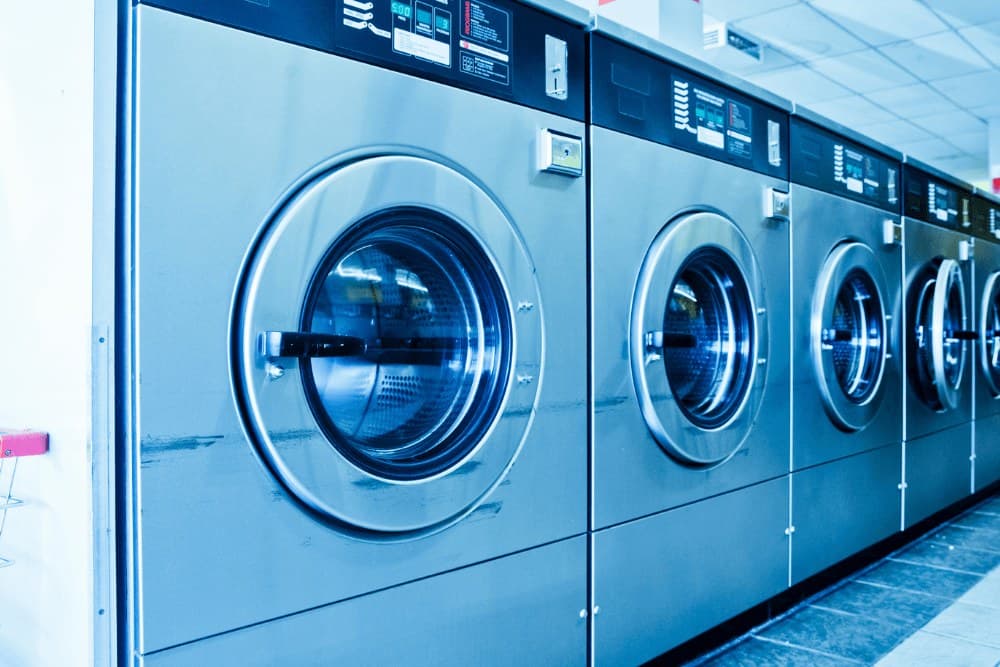 Row of blue-lit industrial front-loading washing machines in a commercial laundry