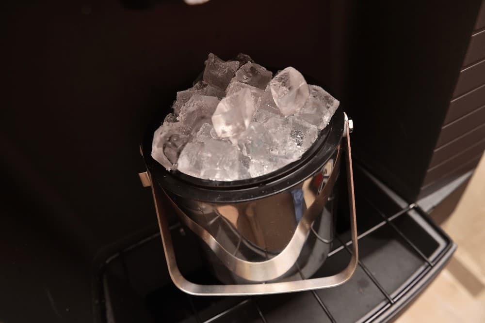 Stainless steel ice bucket filled with clear ice cubes against a dark background