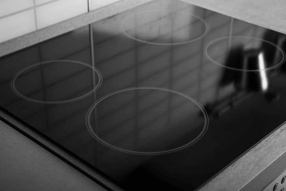 Close-up of a black induction hob's glass cooking surface showing the ring markings for each cooking zone, photographed from directly above with no cracks visible