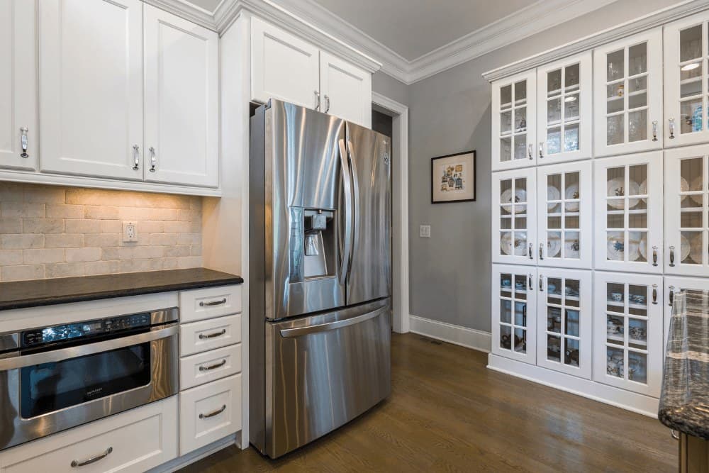 Kitchen with a built-in microwave drawer set into the white cabinetry beside a stainless steel French-door refrigerator
