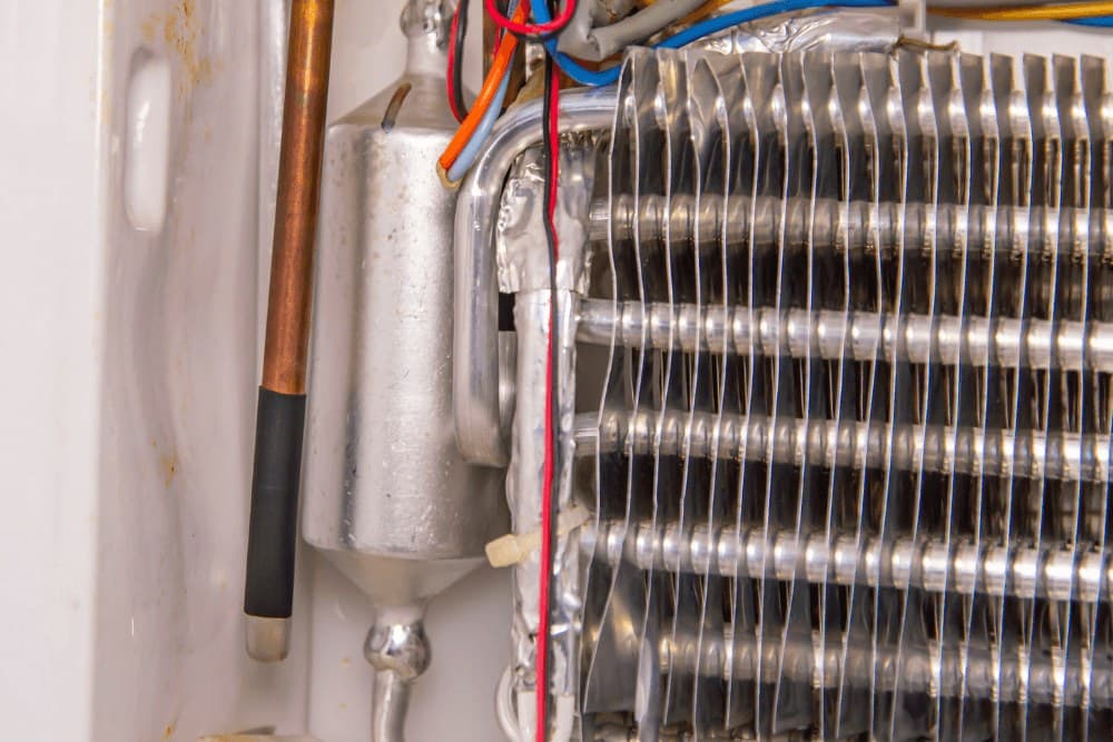 Close-up of an aluminium-finned evaporator coil with copper tubing and wiring inside a refrigeration unit