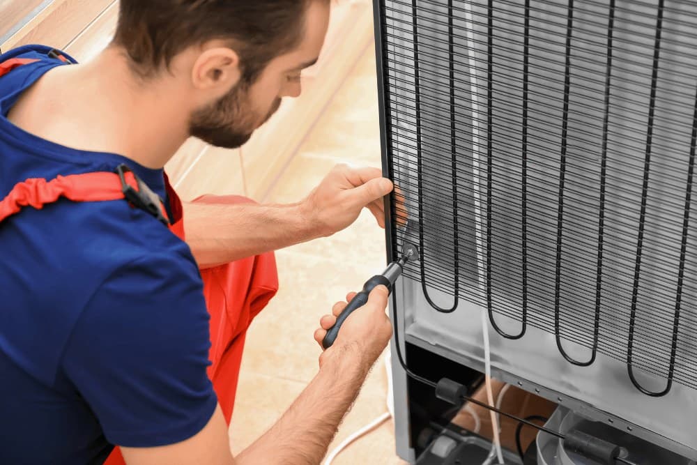 Technician holding a screwdriver against the rear coil of a refrigerator