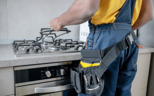 Technician with a tool belt adjusting the grate of a built-in gas hob above a built-in oven